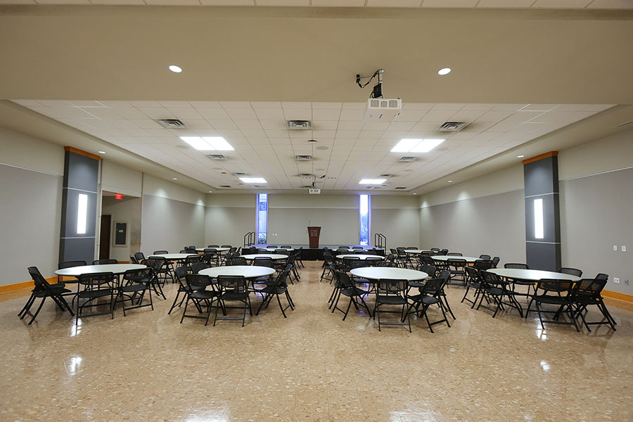 Large multipurpose room with round tables and black folding chairs.