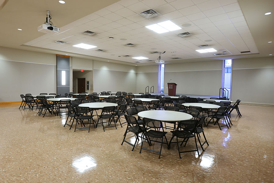 Large multipurpose room with round tables and black folding chairs.
