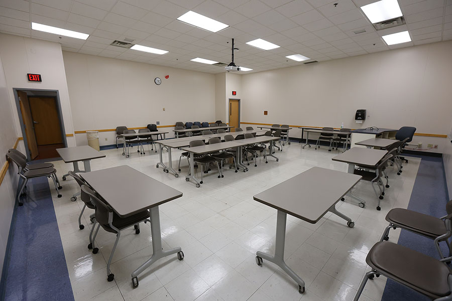 Empty classroom with rows of tables and rolling chairs.