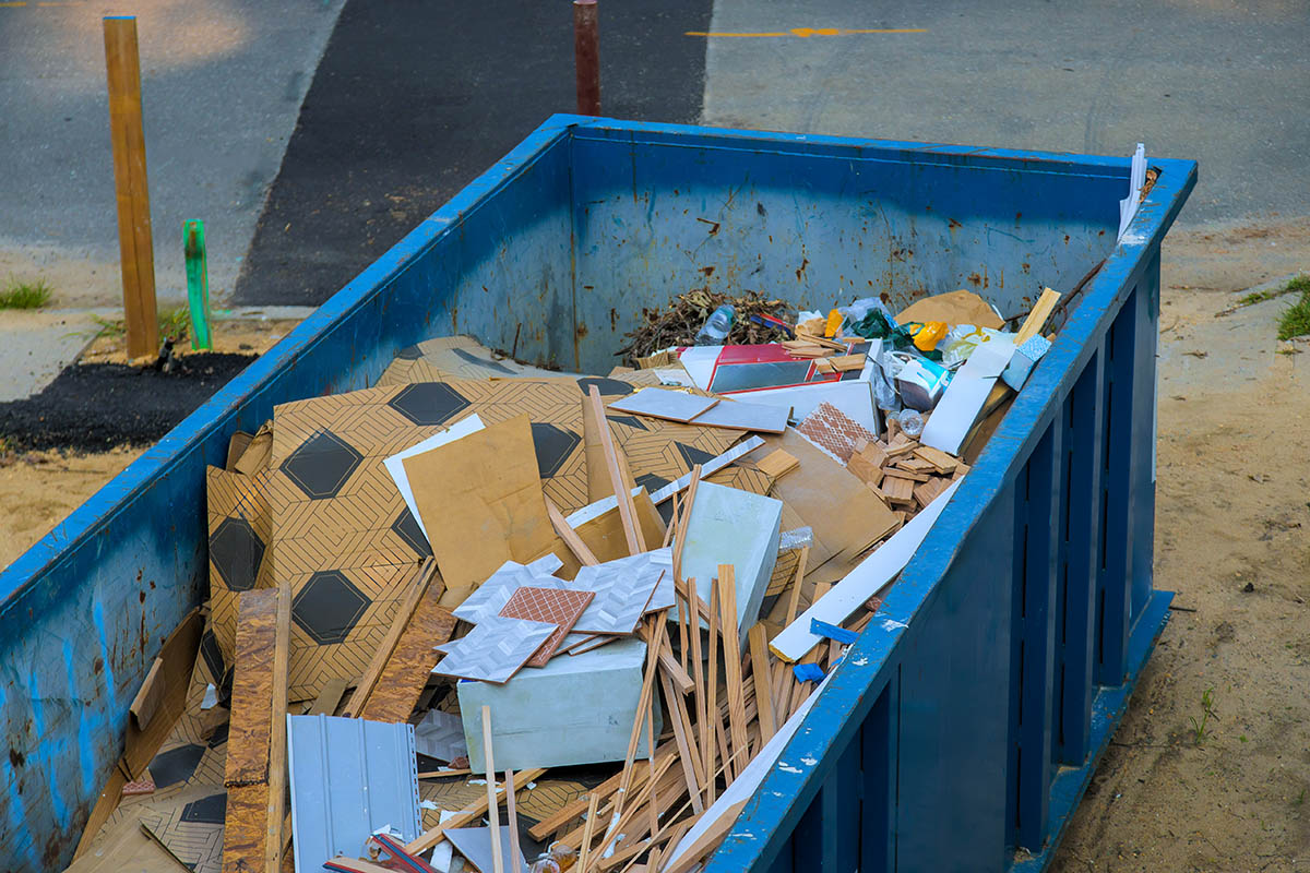 blue dumpster half filled with boxes and paper trash