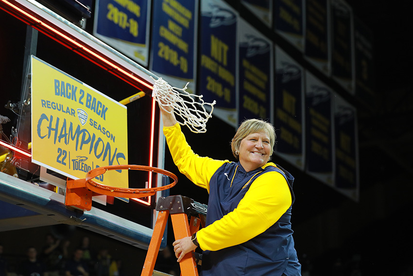 Coach Cullop, the coach of UToledo's women's basketball team, standing on a ladder and grabbing the net from a basketball hoop