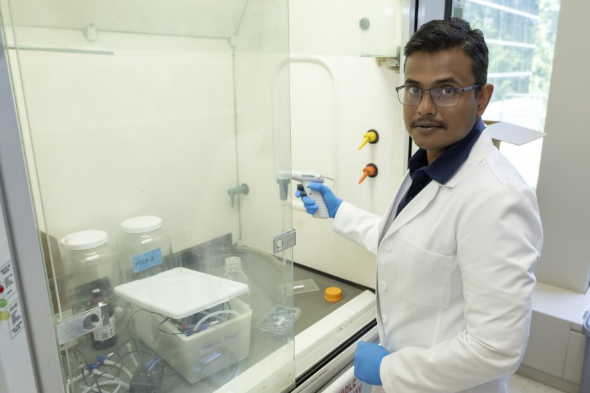 Priyo Goswamee, Ph.D., holding a device in a glass-protected laboratory chamber