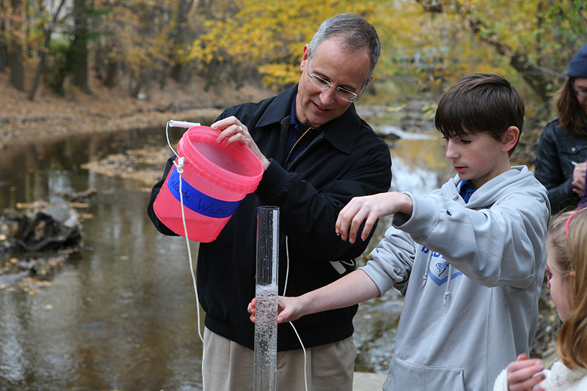 Kevin Czajkowski, Ph.D., working with a bucket and glass tube with a child by a river.