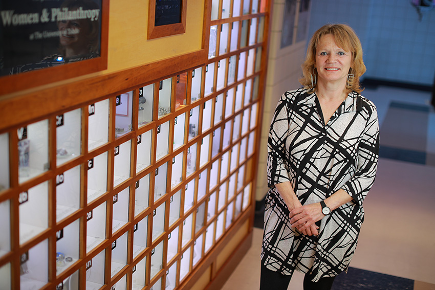 Kristin Kirschbaum, Ph.D., standing in a hallway next to a glass display of elements from the periodic table