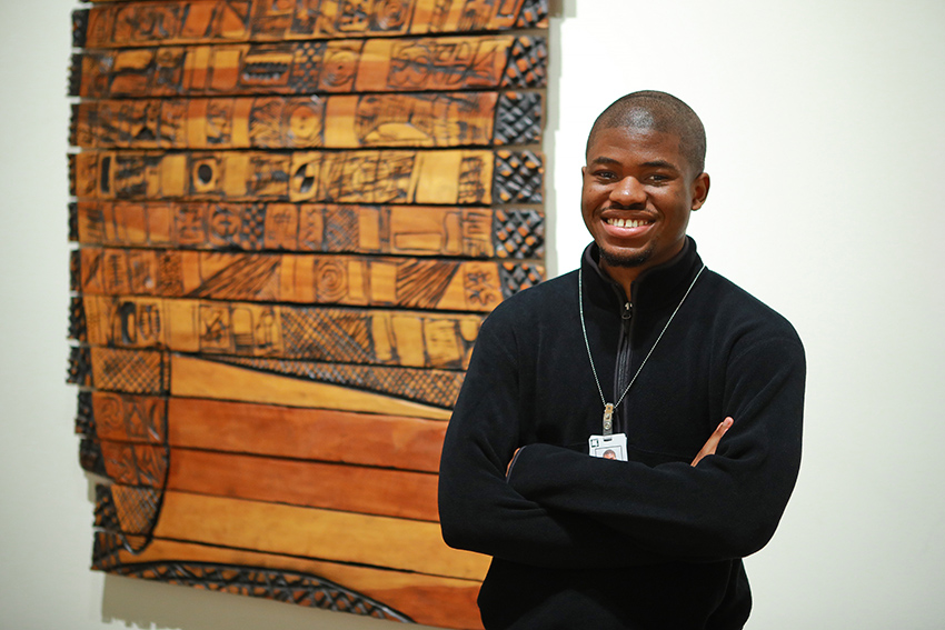 UToledo student Ufuoma Ogbemudje standing in front of a piece of art