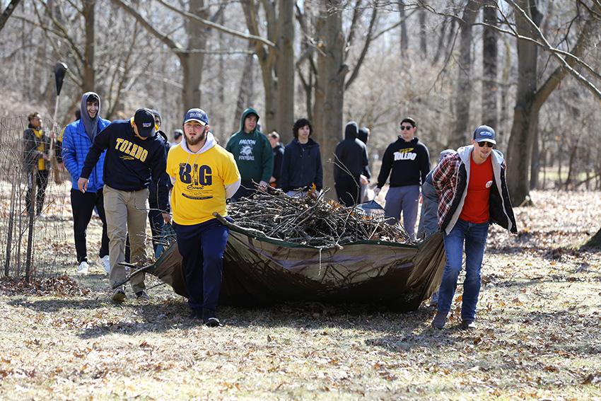 Students working together to haul a tarp holding a large pile of fallen tree branches.