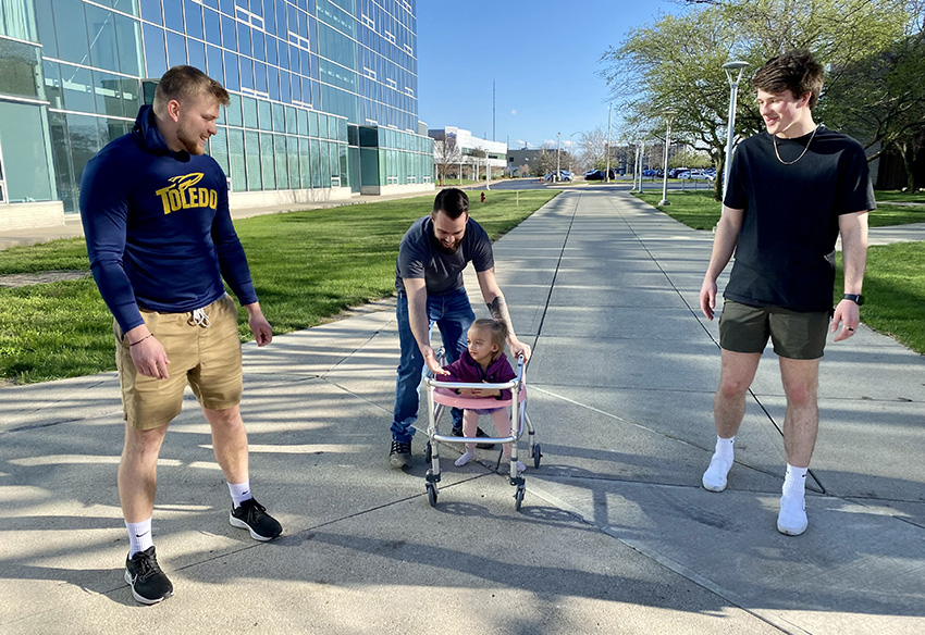 Engineering students guiding a disabled child in a device that assists with walking.