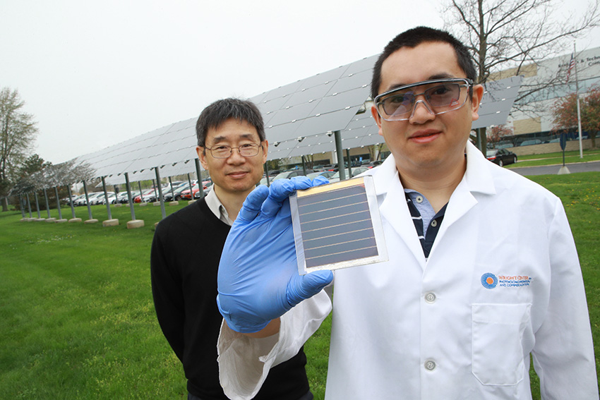 Yanfa Yan, Ph.D., and Zhaoning Song, Ph.D., standing in a field of solar panels. Dr. Zhaoning Song is holding a solar cell up to the camera.