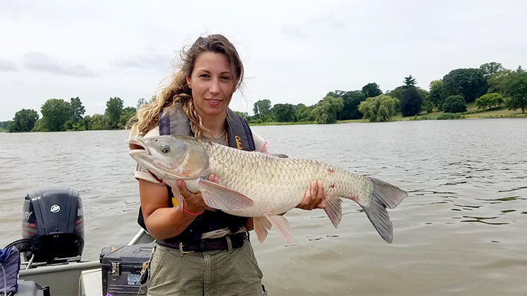 Kaitlen Lang holding a invasive grass carp on a boat in Lake Erie
