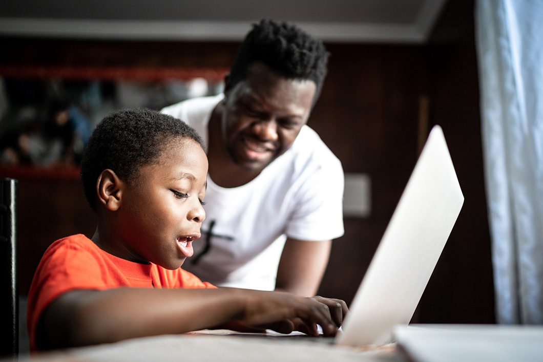 A father watching his son engage in remote learning on a laptop