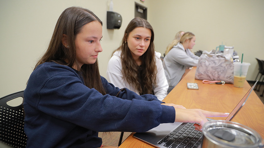 Two students working together on a laptop in a classroom.