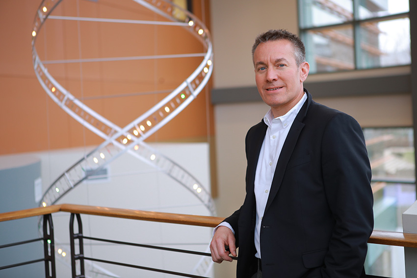 Jason Huntley, Ph.D., standing in front of a sculpture of DNA