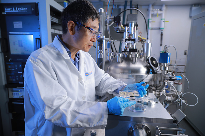 Yanfa Yan, Ph.D., working in a lab with complex machinery, wearing a white lab coat