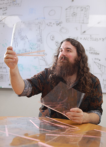 Graduate student Sam Beiler examaning translucent sheets in front of a whiteboard