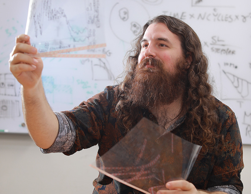 Graduate student Sam Beiler examaning translucent sheets in front of a whiteboard