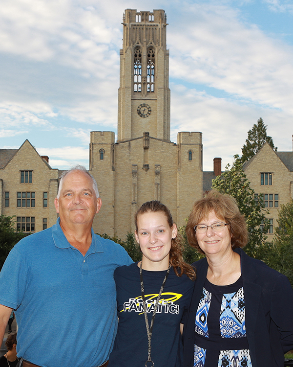 Student standing with her parents in front of University Hall's clock tower
