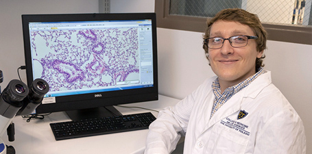 Joshua Breidenbach sitting in front of a computer and microscope in an office