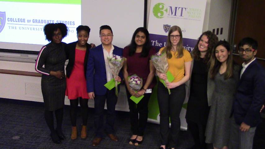 2019 Three Minute Thesis Finalists [8] lined up in front of banner