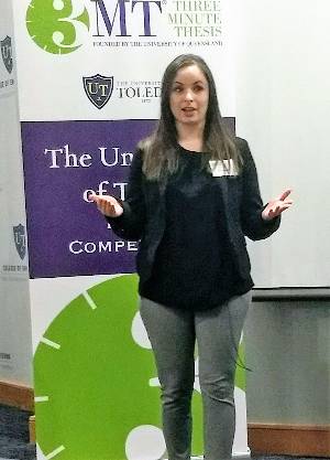 Photograph of Amy Capparelli in front of the 3MT banner delivering her presentation