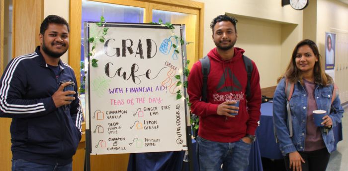 Students standing next to decorated whiteboard with coffee cups in their hands.