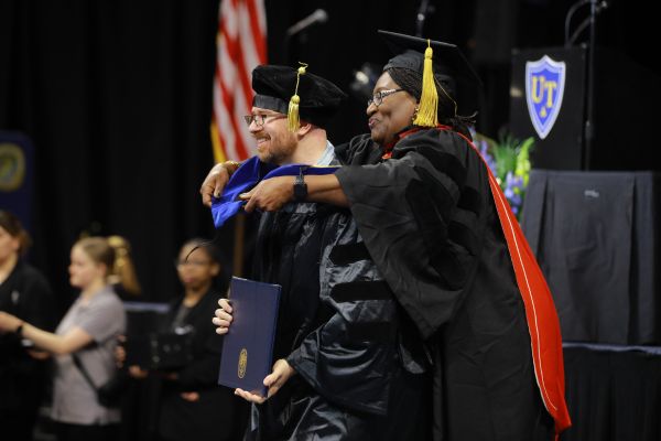 Doctoral candidate in regalia being hooded by advisor