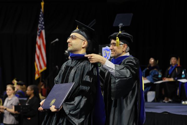 Man in regalia being hooded by advisor during commencement