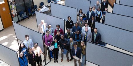MGRS Group Photo Students, facutly and staff smiling and looking up among poster stands at conference