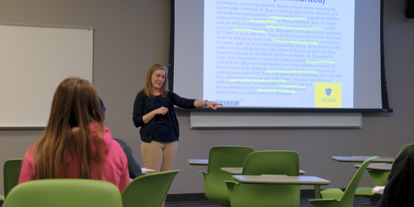 Presenter addressing classroom in front of presentation slide with text