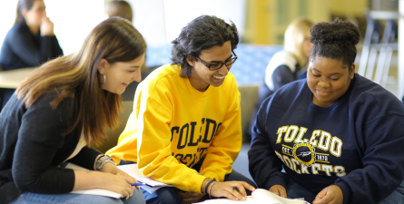 Smiling students sitting at table talking and reading papers in Carlson Library