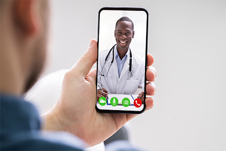 Man's hand holding a phone. phone has an image of a smiling doctor during a telemedicine appointment