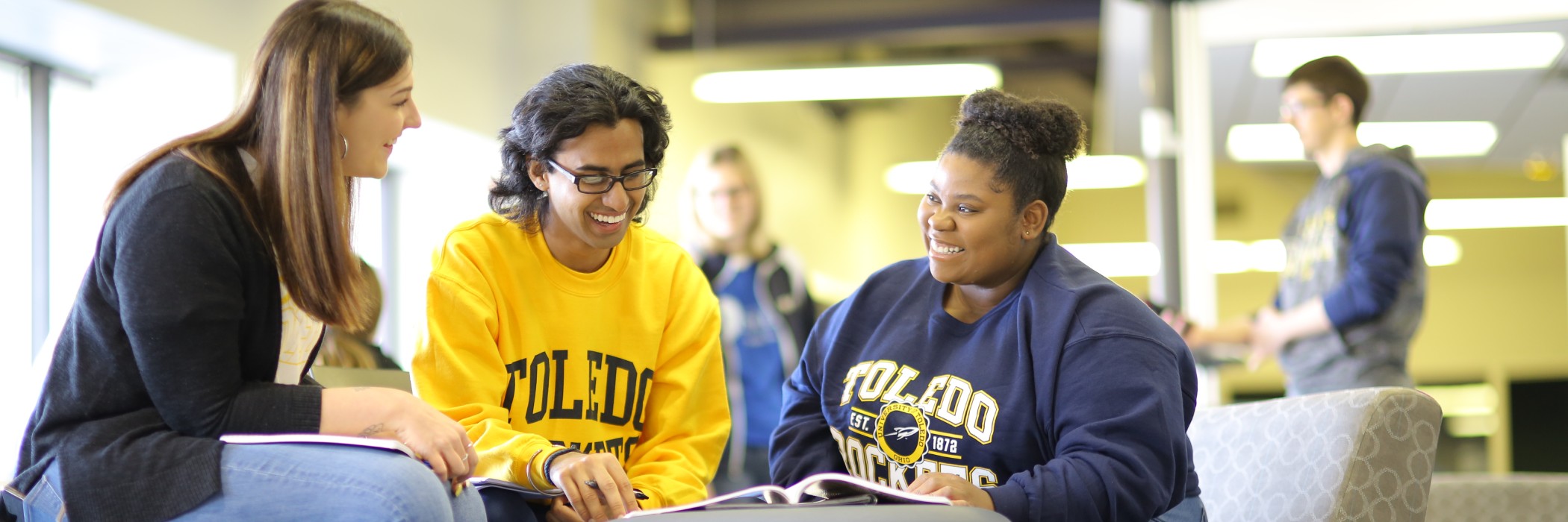 three UToledo students smiling and sitting around a table in the library