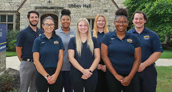 A diverse group of admission counselors standing together on UToledo's campus, smiling at the camera