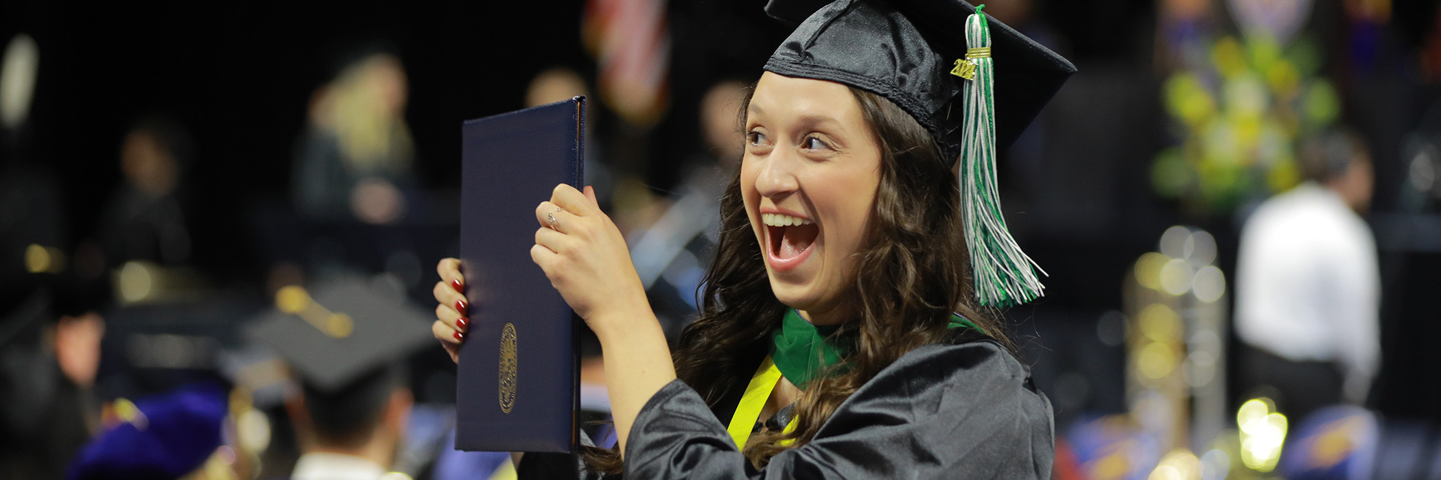 UToledo student at graduation holding up a diploma and smiling 