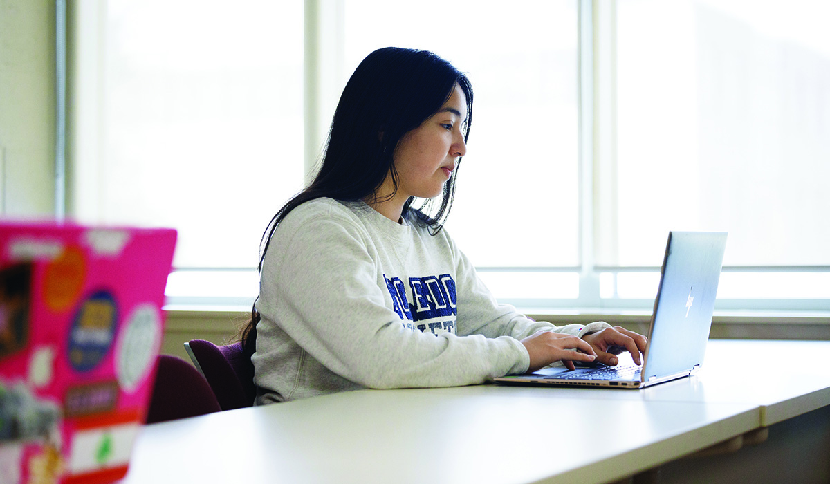 Woman sitting at a desk in a class room using a laptop