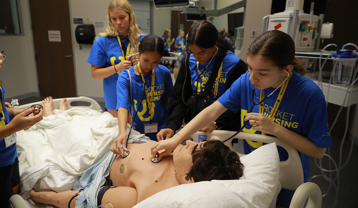Nursing camp students using medical equipment on a test mannequin in a hospital bed