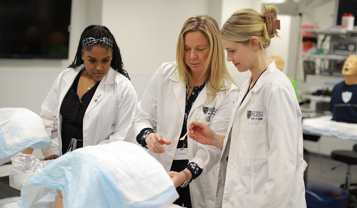 two nursing students and a nursing professor in a lab class room using medical equipment
