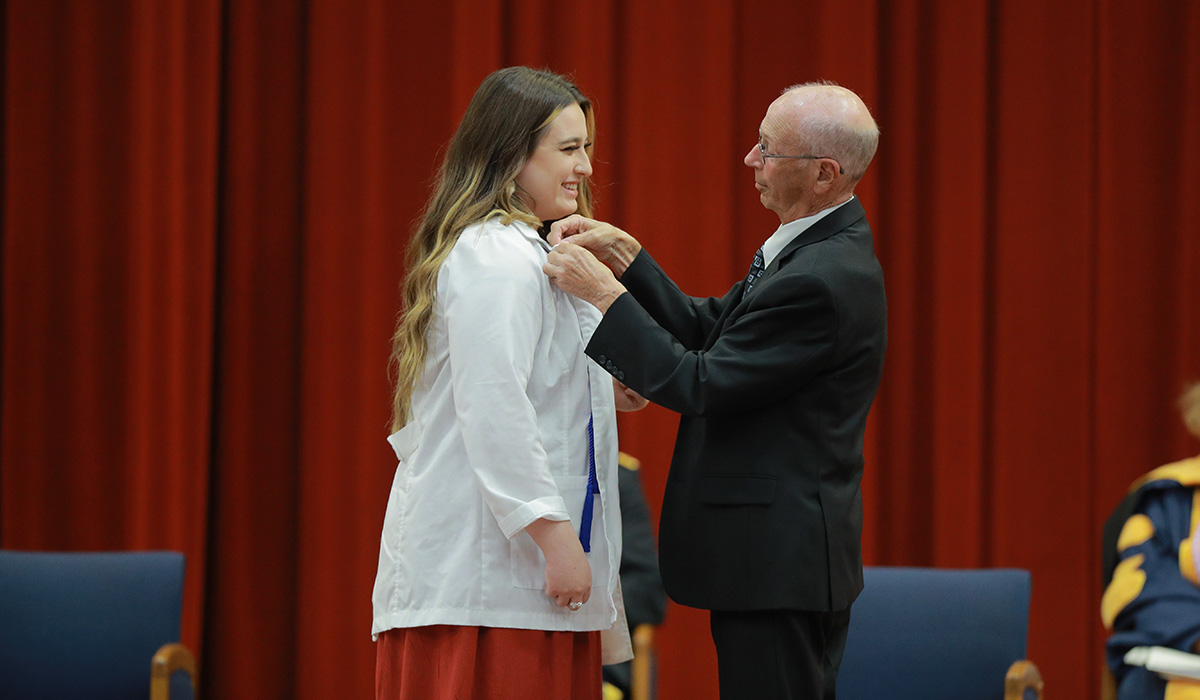 A man putting a pin on a nursing students coat at the pinning ceremony