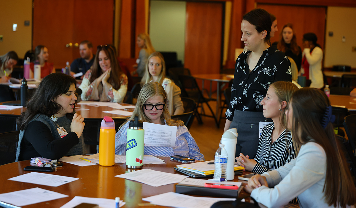 Occupational Therapy Doctorate students at the fall symposium, students are sitting at tables looking at paperwork and talking to symposium staff