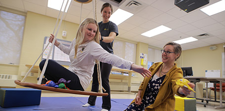 student sitting on a swing reaching for an object the professor is holding