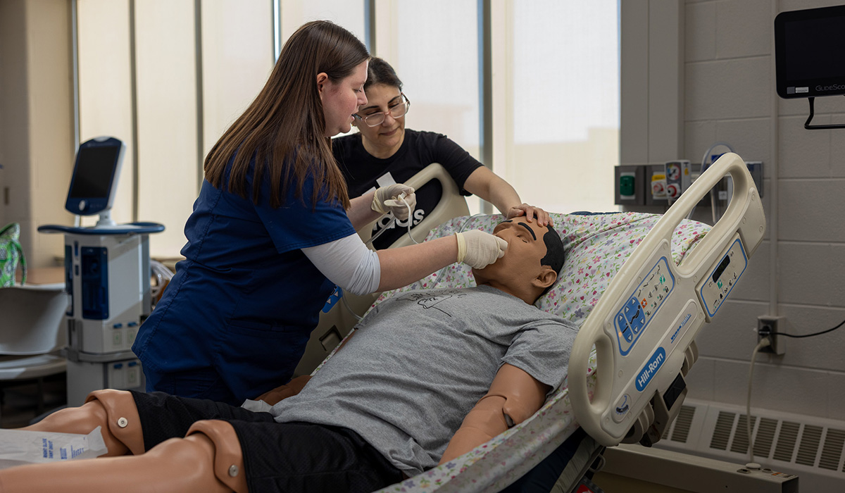 Two Respiratory Care students using medical tools on a practice mannequin in a medical classroom