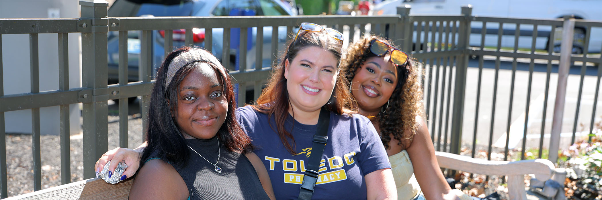 three women sitting on a bench and smiling at homecoming pregame at alumni pavilion