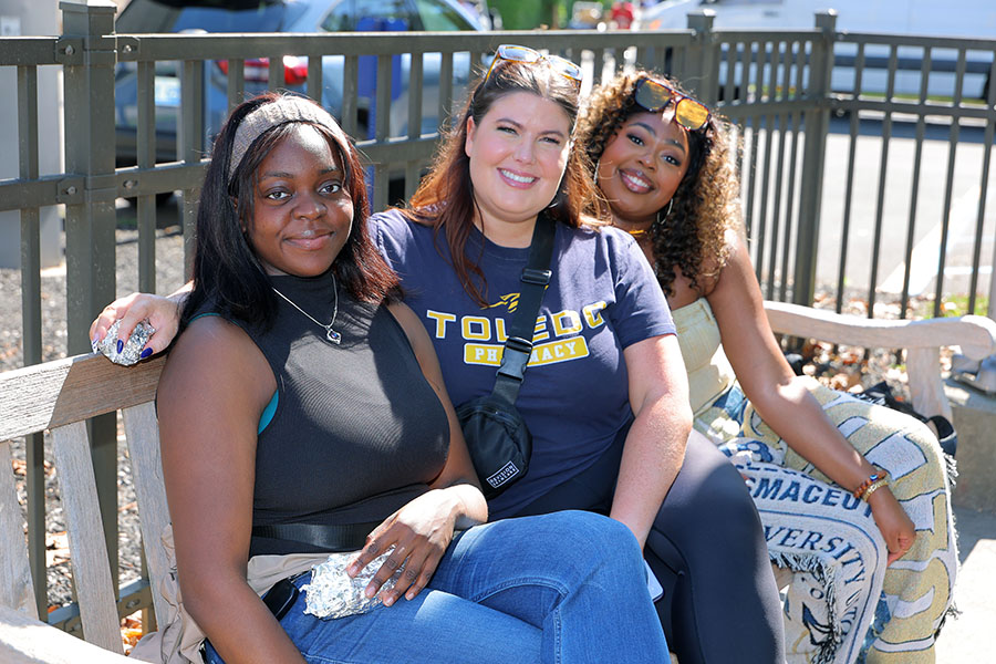three women sitting on a bench and smiling at homecoming pregame at alumni pavilion