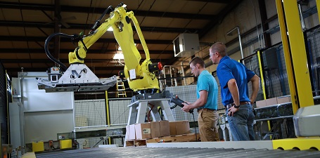 large robotic arm over a conveyor belt with two men standing to the side, observing the machine.