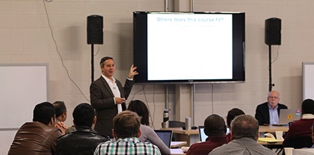 Man lecturing at television in front of large room