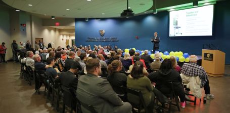 Man in a suit standing on a stage speaking in front of a room full of people at the University of Toledo Business Incubator's Tech419 Pitch Competition.