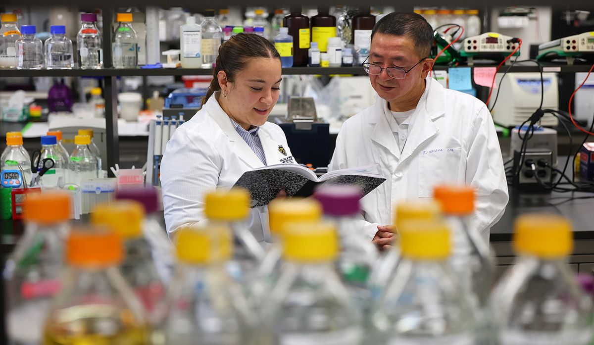 Dr. Jianmin Zhang reviews a document with a student researcher in a laboratory surrounded by research equipment and supplies.