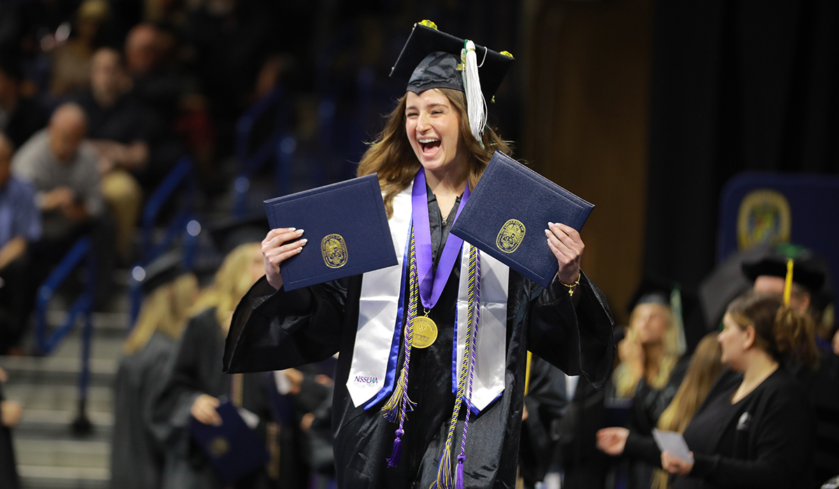 student at graduation holding two diploma's on stage