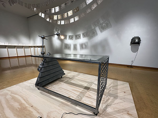 Art gallery with multiple works on display. The main focus is of a metalic table shaped art display that uses many shapes and sizes. 