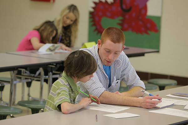 adults sitting at a table with children helping them with school work on papper