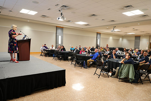 A speaker on a stage standing at a podium talking to a room full of people